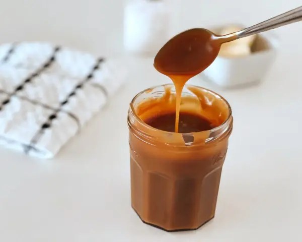 Une cuillère verse du caramel onctueux dans un pot. La recette caramel parfaite pour vos desserts.