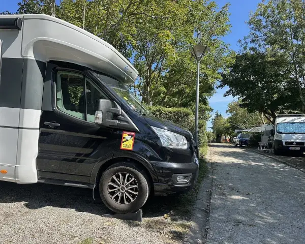 Husbil parkerad på en campingplats vid frankrike kust. Soligt väder med träd och andra husbilar i bakgrunden.