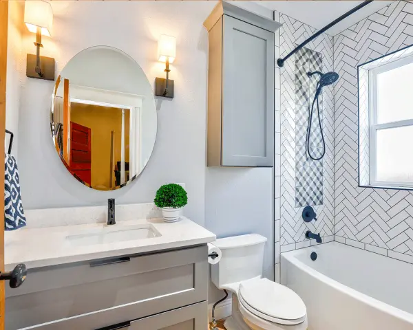 Une petite salle de bain moderne avec baignoire, lavabo gris, miroir rond et carrelage chevrons. Une belle idée pour optimiser l'espace.