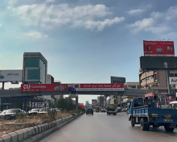 Driving in Lebanon, a busy street with cars, trucks, and billboards advertising various services and products.