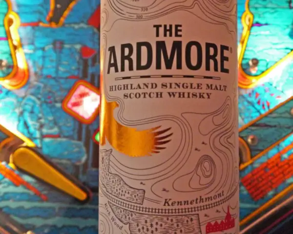 Flasche "The Ardmore" Highland Single Malt Scotch Whisky steht vor einem bunten Flipperautomaten. Ein spannender Ardmore Whisky Test!