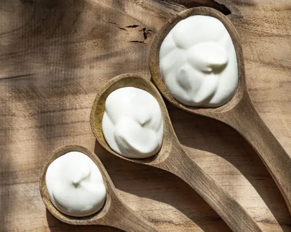 Tre cucchiai di legno pieni di panna da cucina su un tagliere rustico.