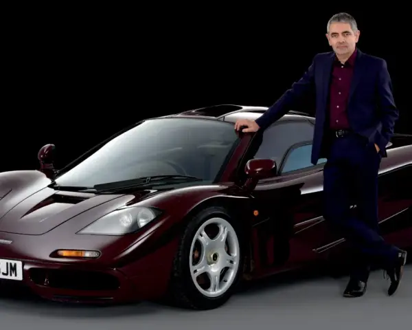 Rowan Atkinson w garniturze opiera się o swój bordowy McLaren F1. To jeden z jego ulubionych samochodów.