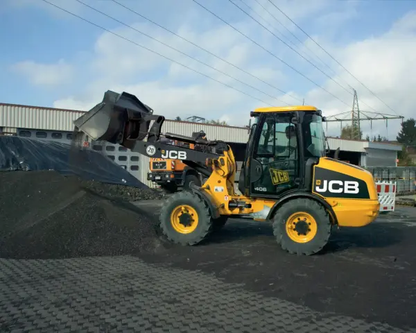 Żółta ładowarka JCB 406 z podniesioną łyżką, gotowa do pracy. Dane techniczne tej maszyny pozwalają na efektywne przenoszenie materiałów.