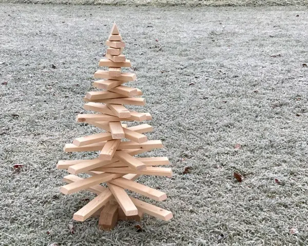 Ein selbstgemachter Tannenbaum aus Holz, der auf frostigem Gras steht. Eine rustikale Deko-Idee, um den Winter zu begrüßen.
