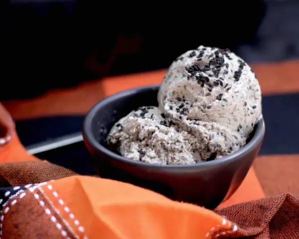 Zwei Kugeln cremiges **black sesame ice cream** in einer Schale, bestreut mit schwarzen Sesamsamen, auf einem karierten Stoff.