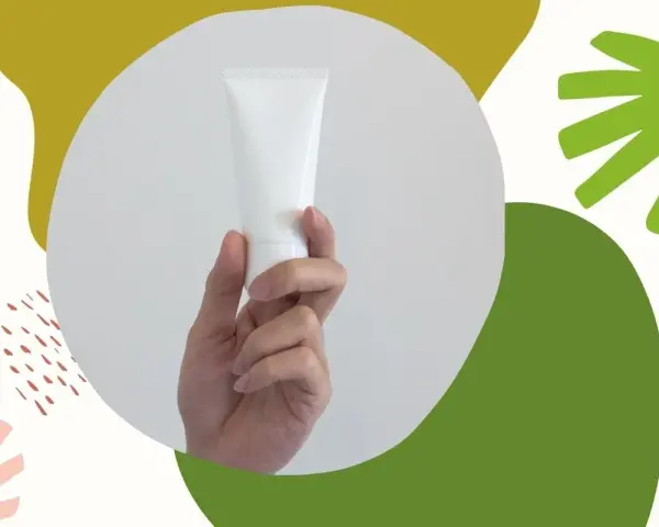 Dłoń trzyma białą tubkę kosmetyku. Czy zawiera alkohol denat w kosmetykach? Abstrakcyjne kształty w tle.