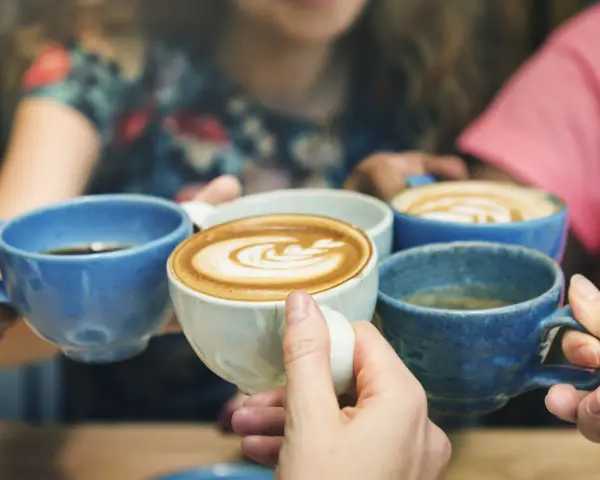 Vier Hände halten bunte Kaffeetassen. Der Kaffee reizt die Blase, aber der Genuss ist es wert.