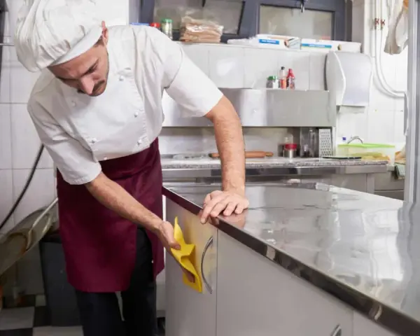 Cocinero con delantal limpiando encimera de acero inoxidable. Esencial para la limpieza de restaurantes.