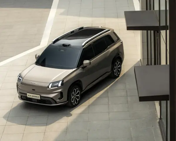 Szary elektryczny SUV GAC Aion V z czarnym dachem i relingami, zaparkowany na zewnątrz.