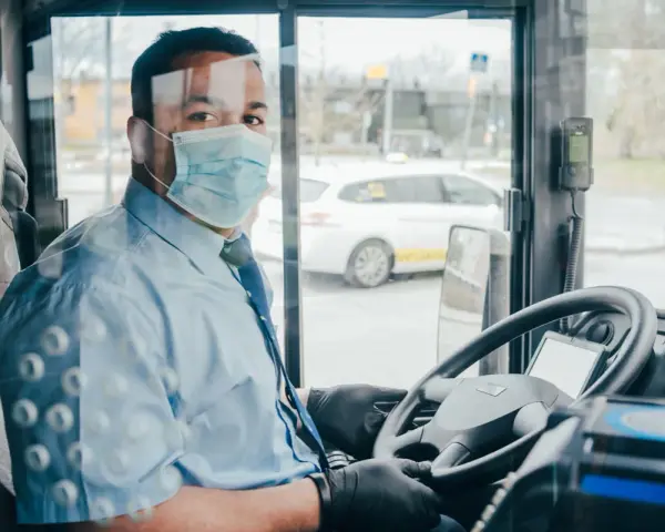 Kierowca autokaru w masce i rękawiczkach za kierownicą. Zapytaj o wynajem autokaru cena.