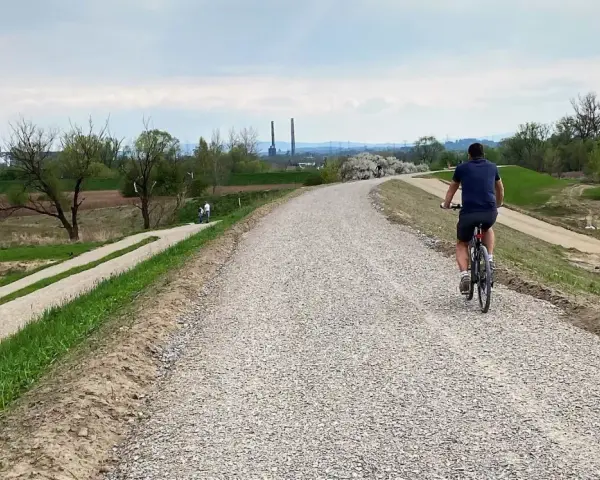 Mężczyzna na rowerze przemierza nową ścieżkę rowerową w Skawinie. W tle widać przemysłowe kominy i zielone tereny.