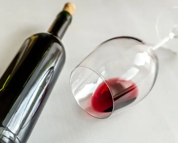 Ciemna butelka i przewrócony kieliszek z czerwonym winem. Idealny wieczór z winem półwytrawnym.