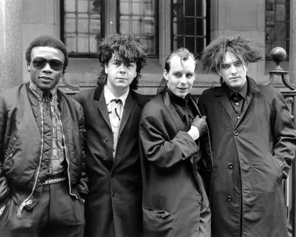 Vier Männer in dunkler Kleidung, Post-Punk-Ästhetik, stehen vor einem Gebäude.