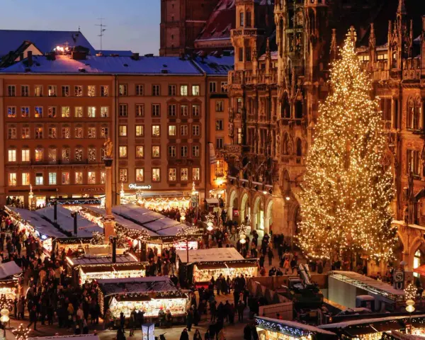 A bustling Christmas market in Munich, Germany, with a towering, illuminated tree and snow-dusted stalls.