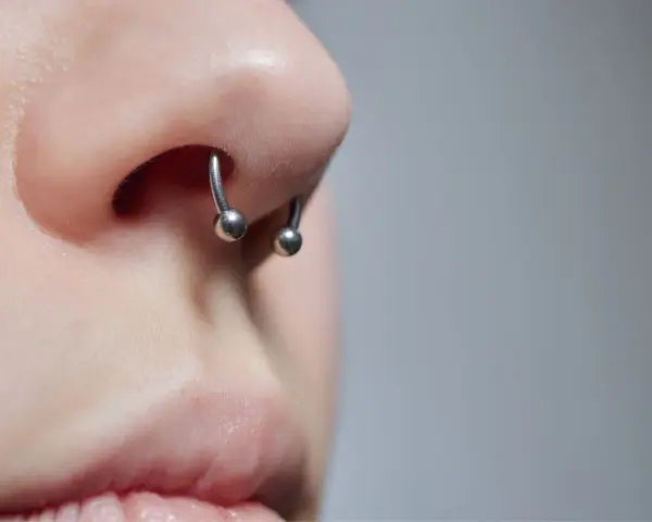 Zbliżenie na nos z kolczykiem typu septril piercing. Metalowy okrąg z dwoma kulkami subtelnie zdobi przegrodę nosową.