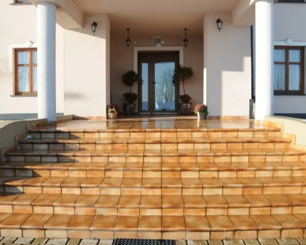 Amplias escaleras exteriores para casas de dos pisos, con escalones de baldosas naranjas que conducen a una entrada principal.