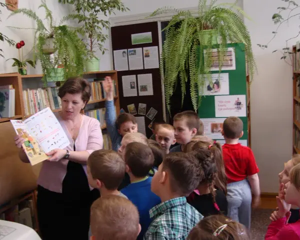 Nauczycielka czyta dzieciom książkę, tworząc inspirujące lekcje biblioteczne scenariusze. Dzieci słuchają z uwagą.