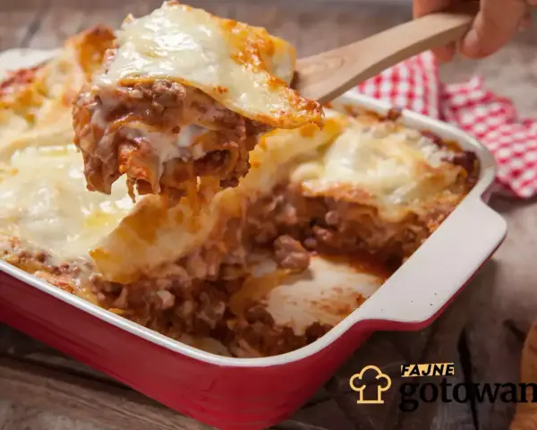 Pyszna, gorąca lasagne z mięsem mielonym i ciągnącym serem, właśnie nakładana drewnianą łopatką. Idealna na rodzinny obiad.