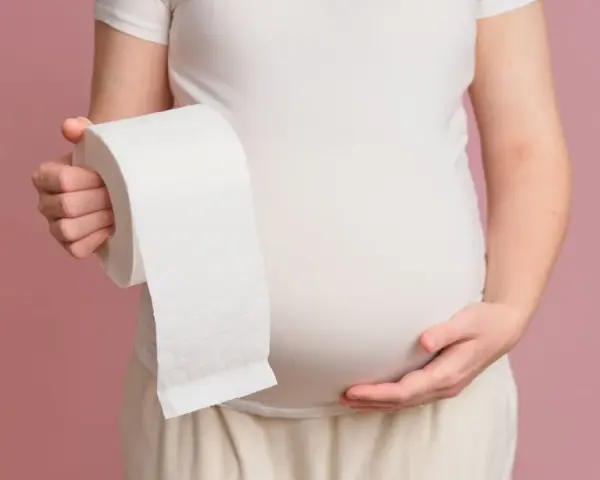 Ciężarna kobieta trzymająca rolkę papieru toaletowego, symbolizująca luźne stolce w ciąży w 1 trymestrze.