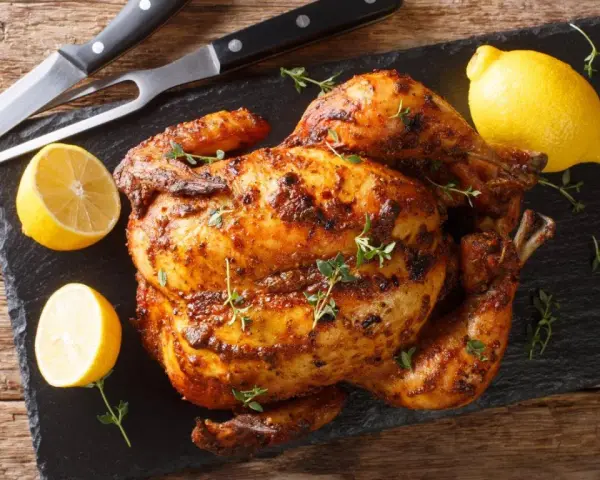 Pollo al horno dorado y jugoso, adornado con tomillo fresco y acompañado de limones cortados. Un festín listo para servir.