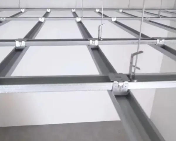 Sufit podwieszany krzyżowy z białymi panelami i metalową konstrukcją. Widać system profili, który tworzy siatkę, a nie pojedyncze belki.