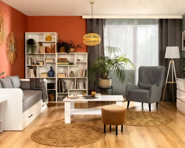 W przytulnym salonie z pomarańczową ścianą stoi biały regał Nepo pełen książek i dekoracji. Obok kanapa, stolik i fotel.