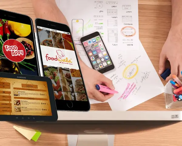 Diseño de apps para restaurantes: teléfonos y tabletas muestran menús y logos. Bocetos y marcadores sugieren planificación.