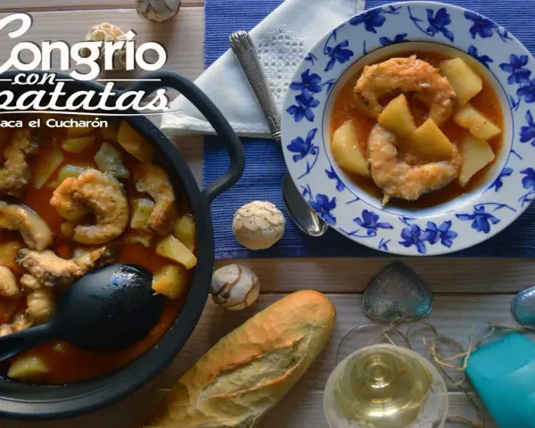 Congrio con patatas, un plato reconfortante servido en cazuela y plato decorado. Acompañado de pan y vino blanco.