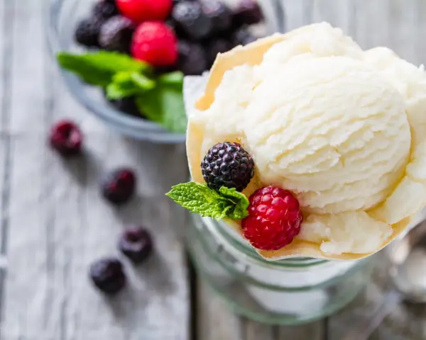 Cremiges Joghurteis selber machen: Eine Portion mit frischen Beeren und Minze, daneben eine Schüssel voller Brombeeren und Himbeeren.