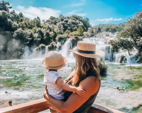 Mama z dzieckiem podziwia wodospady w parku Krka w Chorwacji. Woda jest krystalicznie czysta, a wokół bujna zieleń.