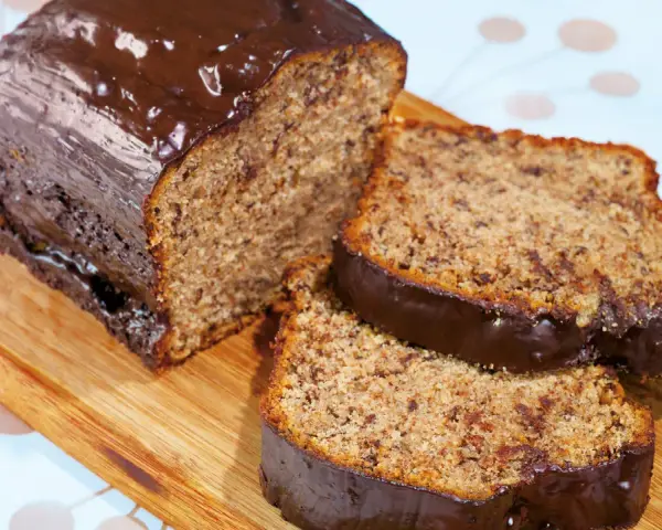 Saftiger Kuchen mit Bananen und Schokoladenglasur, auf einem Holzbrett serviert.