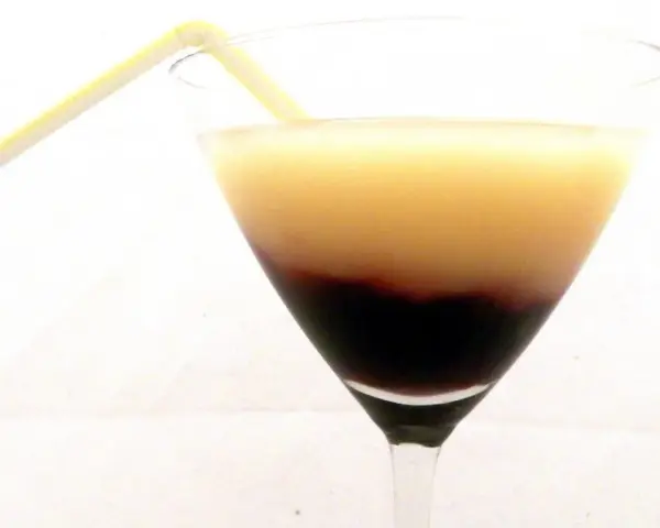 Dwukolorowy drink w kieliszku, z warstwą soku z czarnej porzeczki na dnie i jasnym płynem na górze, ozdobiony żółtą słomką.