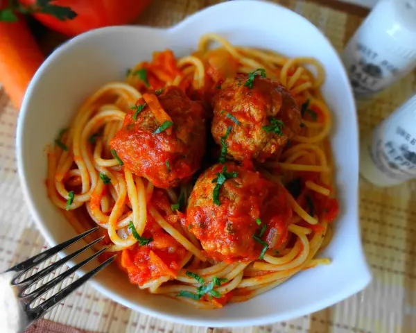 Pyszne spaghetti z klopsikami w sosie pomidorowym, posypane natką pietruszki. Idealne danie dla całej rodziny.