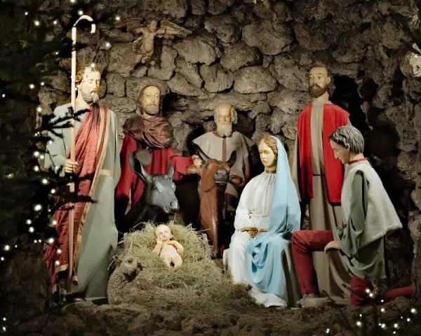 Pasterka w szopce: Święta Rodzina, pasterze i zwierzęta w grocie, ozdobionej światełkami.