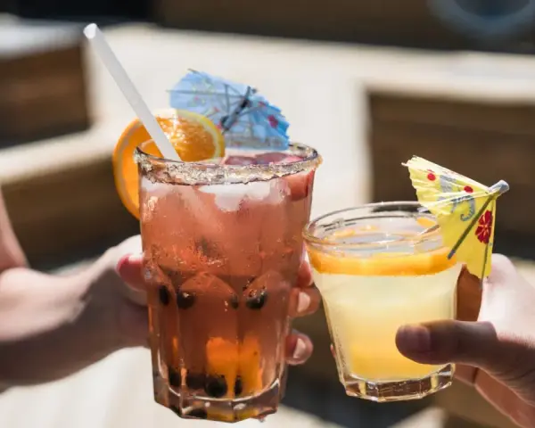 Dwa orzeźwiające drinki, jeden różowy z owocami i pomarańczą, drugi żółty z plasterkiem pomarańczy. Idealne na letnie popołudnie, może z dodatkiem białego wina.
