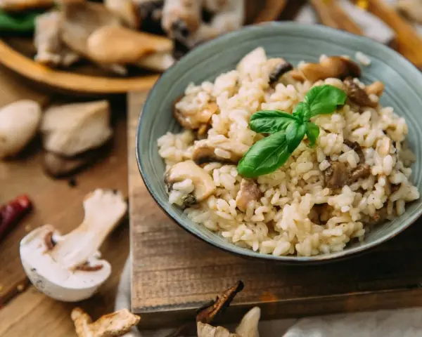 Miseczka kremowego risotto z grzybami i bazylią, otoczona świeżymi grzybami i przyprawami.
