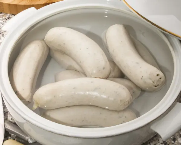 Biała kiełbasa w garnku z wodą, gotowa do parzenia. Delikatne kiełbaski czekają na idealny moment, by trafić na stół.