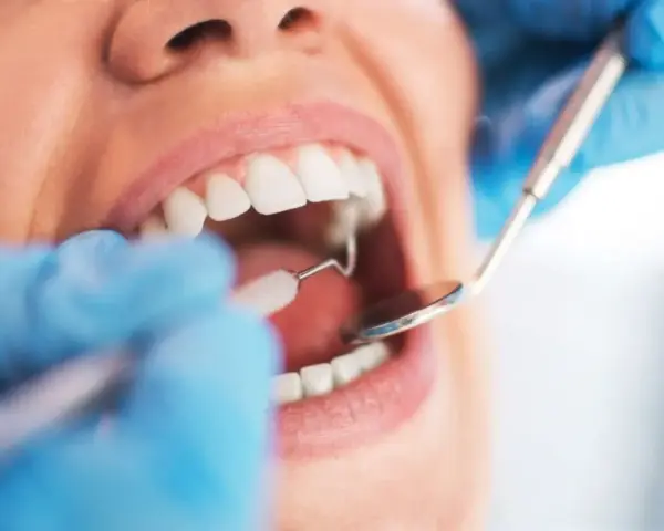 Dentysta wykonuje sanację jamy ustnej, używając lusterka i szczoteczki do czyszczenia zębów.