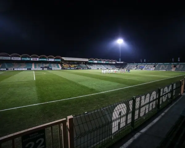Piłkarze na murawie stadionu Górnik Łęczna, oświetlonego jupiterami.