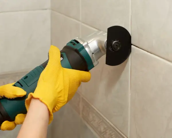 Mit gelben Handschuhen wird eine Fugenfräse benutzt, um Fliesen zu reparieren.