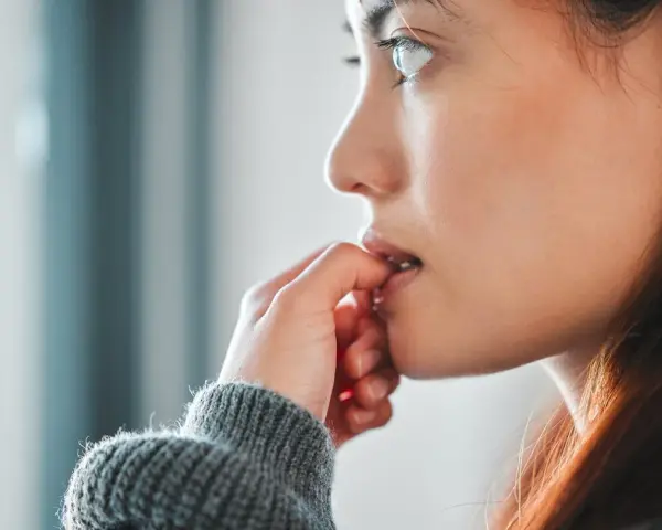 Une jeune femme songeuse, les doigts près de la bouche, réfléchit à comment arrêter de se ronger les ongles.