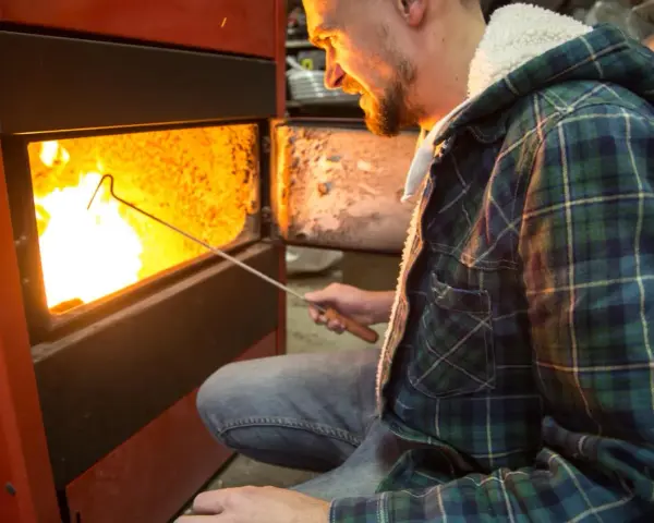 Uomo con camicia a quadri verde accende un fuoco in uno scaldabagno a legna, mostrando come funziona.
