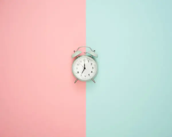 Wecker auf rosa und blauem Hintergrund. Zeit für Stundenreduzierung Schwangerschaft Gehalt.