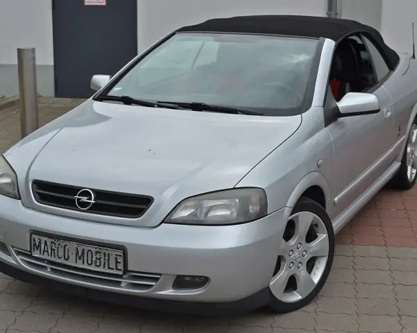 Silberner Opel Astra Bertone Cabrio mit offenem Verdeck, bereit für eine Spritztour.