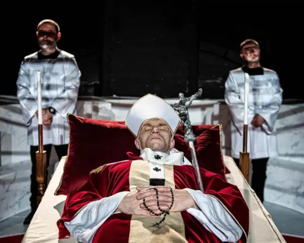Papież w stroju, z różańcem, leży w trumnie. Obok stoją dwaj mężczyźni w białych szatach. Czy to bluźnierstwo, co to?