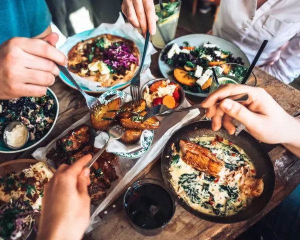 Leckeres Essen in einem Restaurant in Berlin Mitte: Pizza, Lachs, Rippchen und Salate werden von mehreren Händen geteilt.