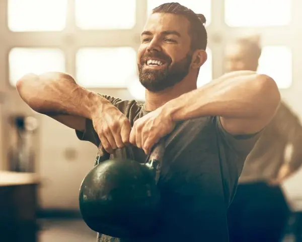 Un homme souriant effectue un exercice kettlebell, concentré sur son entraînement.