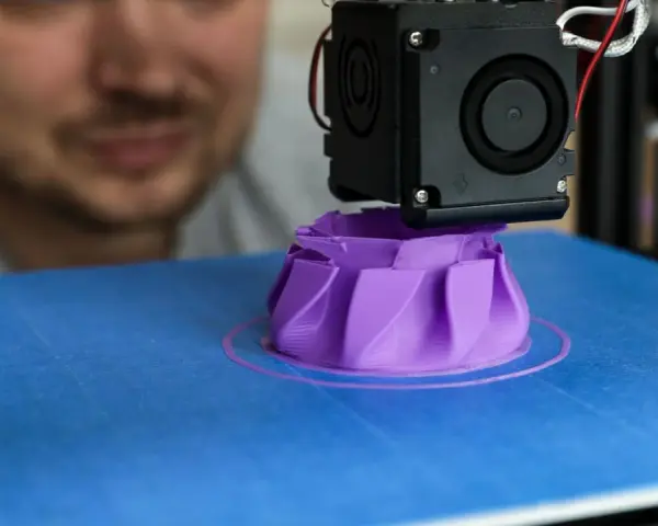 A man watches his 3D printer create a purple object, showcasing its precise 3D printer specifications in action.
