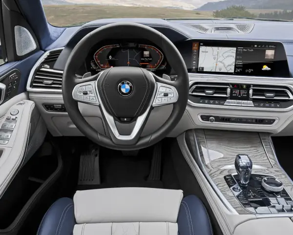 Wnętrze BMW X7: kierownica, ekran multimedialny z nawigacją i muzyką, panel klimatyzacji, dźwignia zmiany biegów.